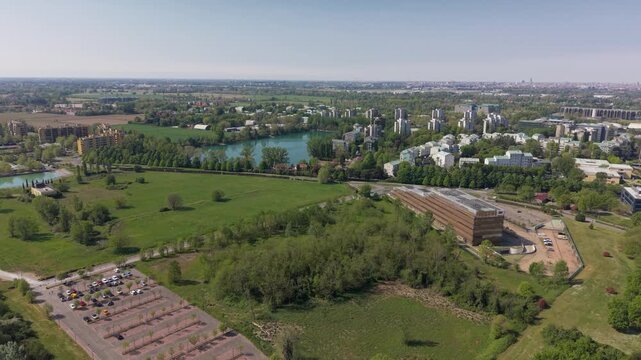 Urban Green Oasis: An aerial view captures the harmonious blend of nature and urban development, with a tranquil lake, lush green parkland, and modern buildings coexisting under a clear blue sky.