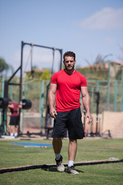 Outdoor CrossFit fitness workout with muscular man training with battle ropes in a sunny park gym
