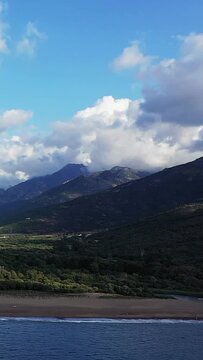 Scenic view of the Delta du Fango with lush green mountains, sandy beach, and dramatic clouds under a blue sky. Natural beauty and tranquility in Corsica.