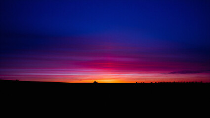 Fototapeta premium Sunset with deep blue and purple sky above silhouetted landscape evening glow colorful atmosphere