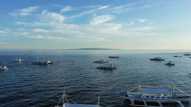Several traditional outrigger boats float on the tranquil blue waters near Panglao, Philippines, under a clear sky with distant land visible on the horizon.