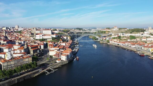 A scenic aerial view of Porto, Portugal, featuring the iconic Dom Luis I Bridge spanning the Douro River under a clear blue sky.
