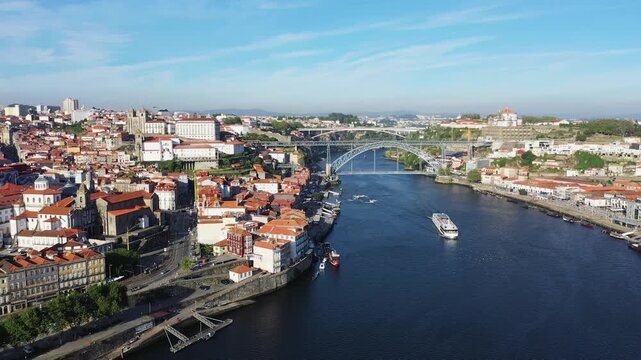 A scenic aerial view of the Dom Luis I Bridge spanning the Douro River in Porto, Portugal, with historic city architecture and boats on the water.