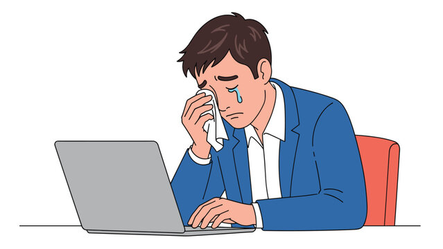 Sad young businessman in a blue suit sits at his laptop and wipes tears from his eyes with a white tissue while crying.