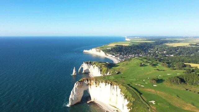 Scenic aerial shot of the dramatic white chalk cliffs and lush green landscape along the coast of Etretat, Normandy, France on a clear summer day.