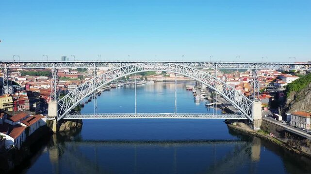 Aerial view of the Dom Luis I Bridge spanning the Douro River in Porto, Portugal, with cityscape and clear blue sky in the background.