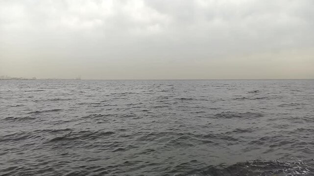 Ocean waves surface view showing the vast dark blue water horizon under a cloudy grey sky during a calm and peaceful day on the open sea for nature background