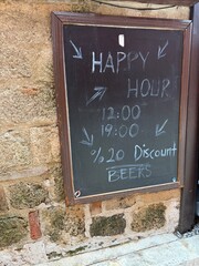 Chalkboard sign displaying happy hour times and beer discount outside on rustic stone wall © dvoevnore