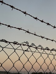 Barbed wire and fence silhouetted against a soft gradient sky background at sunset © dvoevnore
