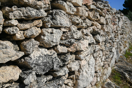 Dry-stone wall constructed from irregularly shaped and unmortared stones. Stone wall, close up. 