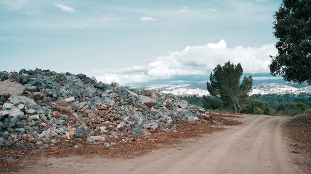 A large pile of rubble and debris sits beside a dirt road in a natural landscape