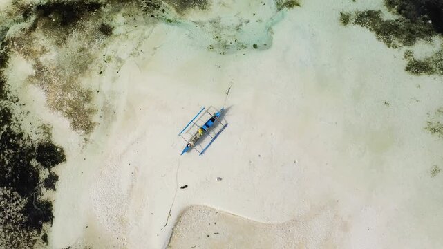 Drone shot of a traditional outrigger boat resting on a white sandbar surrounded by shallow turquoise water on Siquijor Island, Philippines.