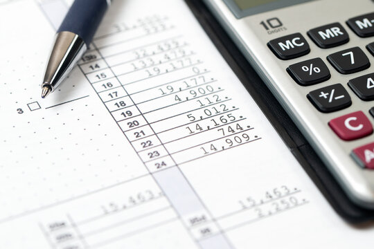 A tax document with various numerical entries and lines, paired with a silver calculator and a blue ballpoint pen.