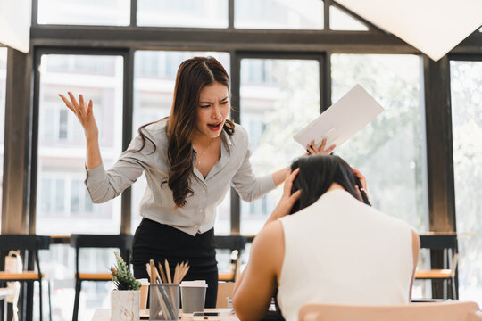 Angry female boss scolding a stressed employee over workplace conflict in a modern office setting