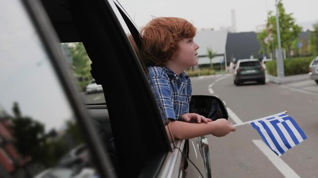 Little boy with Greece flag in the car, looking on the street. Slow motion