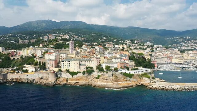 Scenic aerial view of Bastia with colorful historic buildings, marina, and mountains in the background on the coast of Corsica, France.