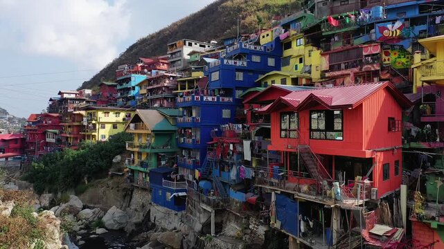 Vibrant, multicolored houses clustered on a hillside in the Valley of Colors, Baguio, Philippines, under a partly cloudy sky.