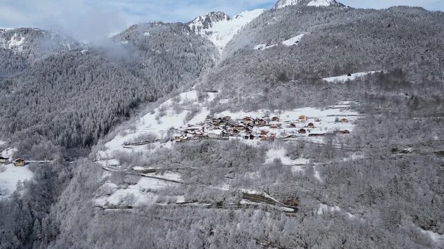 Aerial view of a snowy alpine village with chalets in Tarentaise Valley surrounded by forest and mountains in the French Alps, Savoie, France.
