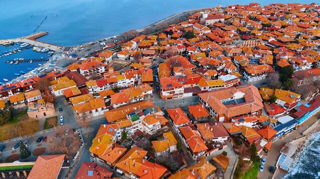 Aerial view of ancient town peninsula with red tiled roofs. Drone shot of coastal city architecture featuring traditional red roofs and harbor in daylight.