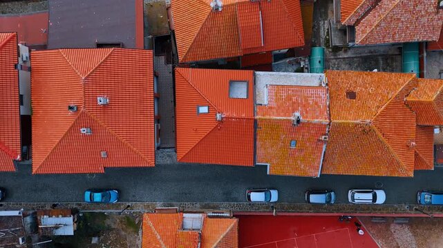 Aerial top down view of red tiled rooftops. Overhead perspective of urban buildings and parked cars on street
