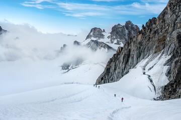 Fototapeta premium Group of climbers hiking on snowy mountain ridge with rocky cliffs in alpine landscape. Mont Blanc Monte Bianco Alps mountain in Europe
