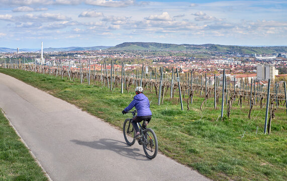 Active senior woman riding an electric mountain bike through vineyards above Stuttgart, Germany. Enjoying spring sunshine with scenic city views, green hills, and a peaceful countryside atmosphere.