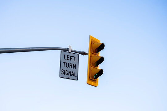 Traffic light with left turn signal sign mounted on a street pole against a clear blue sky. Minimal urban composition highlighting road safety, traffic control, and transportation infrastructure. Humb