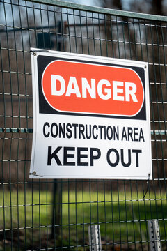 Warning sign reading danger construction area keep out mounted on a metal fence at a restricted site. Safety signage highlighting hazard awareness, site security, and construction regulations in an ou