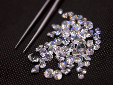 Loose diamonds and gemstones with jeweler's tweezers on dark fabric background for luxury jewelry design