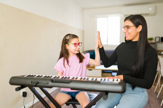 Music teacher and student giving high five during successful piano lesson, learning keyboard skills