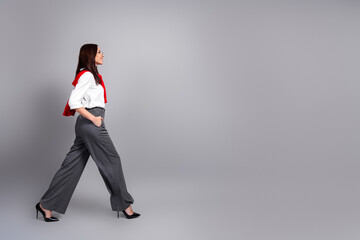 Confident businesswoman walking across neutral studio background in pinstripe trousers, white...