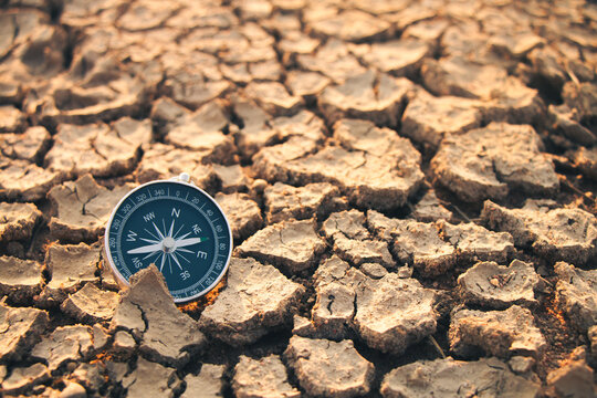 The compass needle on the dry land indicates the need to find a way out of the drought.