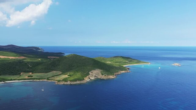 Scenic aerial view of Plage de Tamarone with turquoise waters, lush green hills, and anchored sailboats along the coastline in Corsica, France.