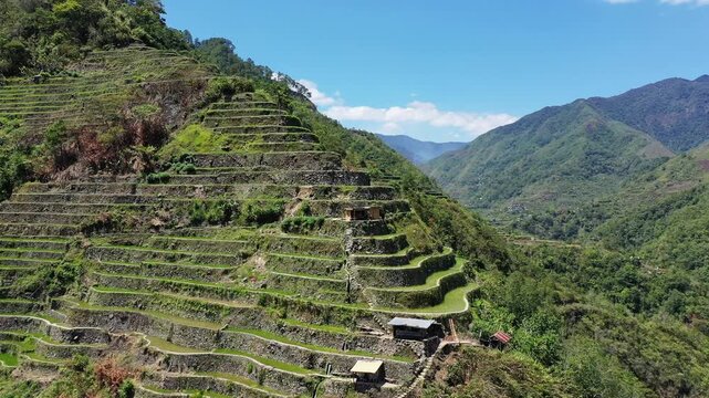 Aerial view of the iconic Batad rice terraces surrounded by green mountains under a clear blue sky in the Philippines.