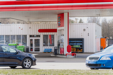 White and red filling station with pump island, shop entrance and cars in foreground, fuel retail, road transport and consumer service theme © K