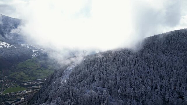 Aerial view of Tarentaise Valley with highway, alpine villages and snowy mountains covered in fog in the French Alps, Savoie, France.