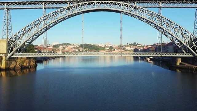Wide view of the Luis I Bridge spanning the Douro River with the cityscape of Porto, Portugal in the background under clear blue sky.