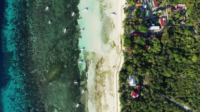 Drone shot of a tropical coastline on Panglao Island, Philippines, showing clear turquoise water, traditional boats, sandy beach, and lush greenery.