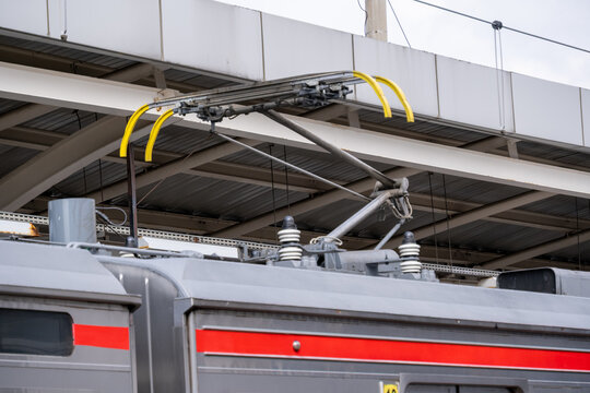 Close-up of a commuter train pantograph mounted on a carriage roof, collecting electric current from overhead lines in an electrified railway system.
