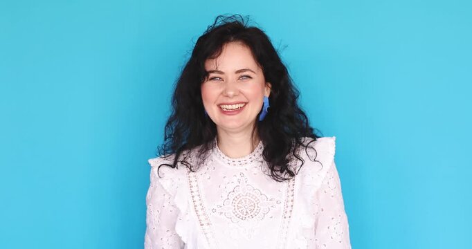 Young woman in white lace dress playfully shaking fist and threatening with smile, saying "I'll show you!" in friendly and caring manner like scolding a child against blue studio background
