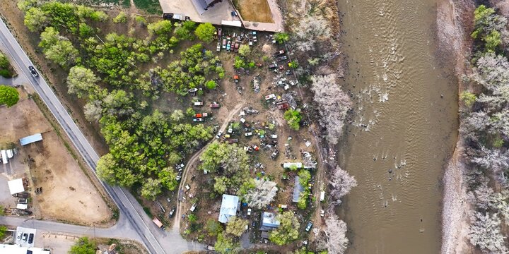 Aerial view of a river flowing with a collection of old cars nestled among verdant trees on its banks, contrasting with the muddy waters, Palisade, Colorado, USA.