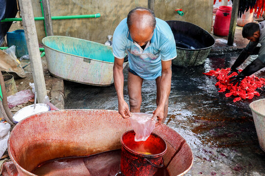 Narayanganj, Bangladesh - 29 March 2026: View of a man in a vibrant scene, dyeing fabric in colorful tubs, the scene bathed in warm sunlight, creating a striking contrast of textures and tones.