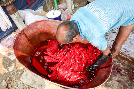 Narayanganj, Bangladesh - 29 March 2026: View of a man immersed in a vivid tableau of crimson-soaked fabrics within a large metal container, a stark contrast to the mundane surroundings.