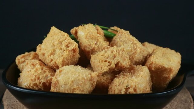 Crispy fried tofu tahu Sumedang in black plate with green chilies on wooden table. Turning.