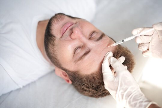 Doctor injecting medication into male forehead. Close-up of cosmetic anti-aging procedure, botox treatment and aesthetic medicine concept in clinic.