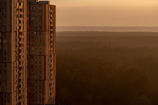 Aerial view of towering apartment blocks casting long shadows over a dense forest shrouded in a golden mist during the early morning light, Kyiv, Kyiv city, Ukraine.