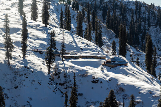 View of snow-blanketed slopes dotted with evergreen trees and humble dwellings, a serene winter scene unfolds in Lasdana, Azad Kashmir, Pakistan.