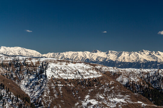 View of snow-dusted mountains under a clear blue sky create a serene winter landscape, the peaks contrasting with the dark slopes, Lasdana, Azad Kashmir, Pakistan.