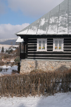 View of a charming dark wood and stone house with snow-dusted roof and bright window boxes nestled in a winter landscape, Donovaly, Slovakia.