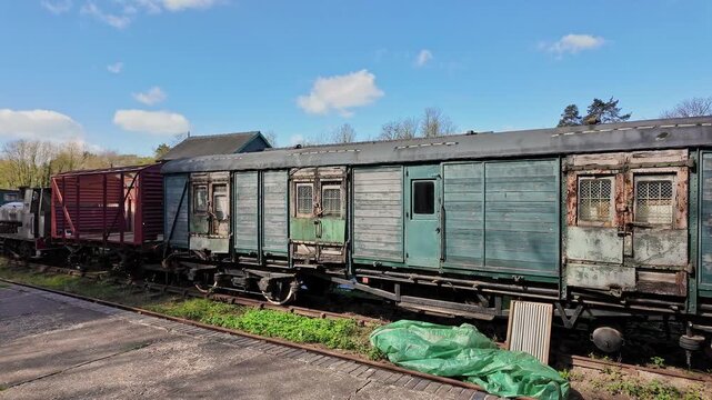 Dilapidated wooden railway carriages stand forgotten in a quiet shunting yard, their warped panels cracked and splintering with age.  Panning shot.